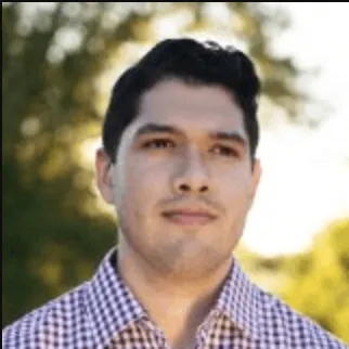 Portrait of a man with short dark hair wearing a checkered shirt with blurred trees in the background.