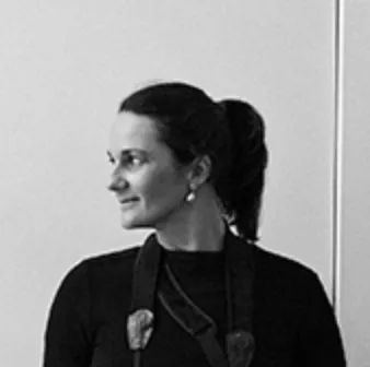 Black and white photo of a woman with dark hair tied back, wearing earrings and a dark top, looking to her left.