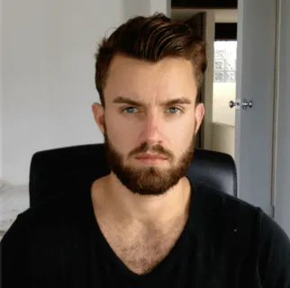 Serious man with beard and short brown hair wearing a black V-neck shirt sitting on a black chair.