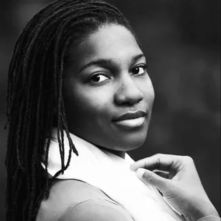 Black and white portrait photo of a woman with long braided hair looking over her shoulder.