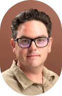 Headshot of a man with short dark curly hair and glasses wearing a brown checkered shirt against a brown background.