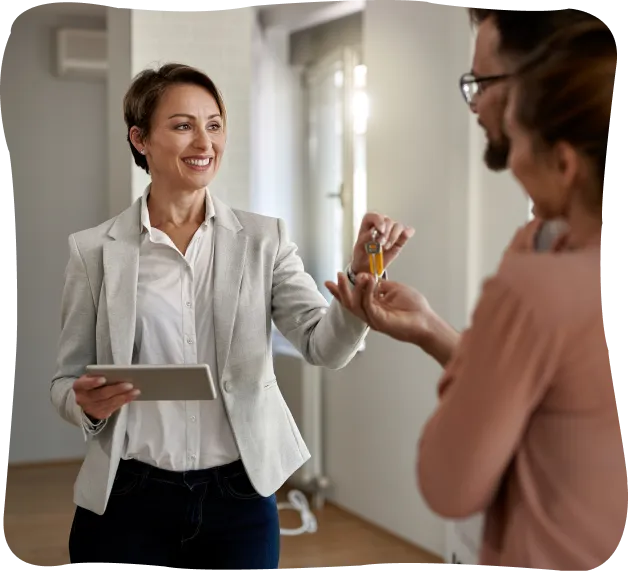 Smiling real estate agent handing over house keys to a couple inside a bright home.
